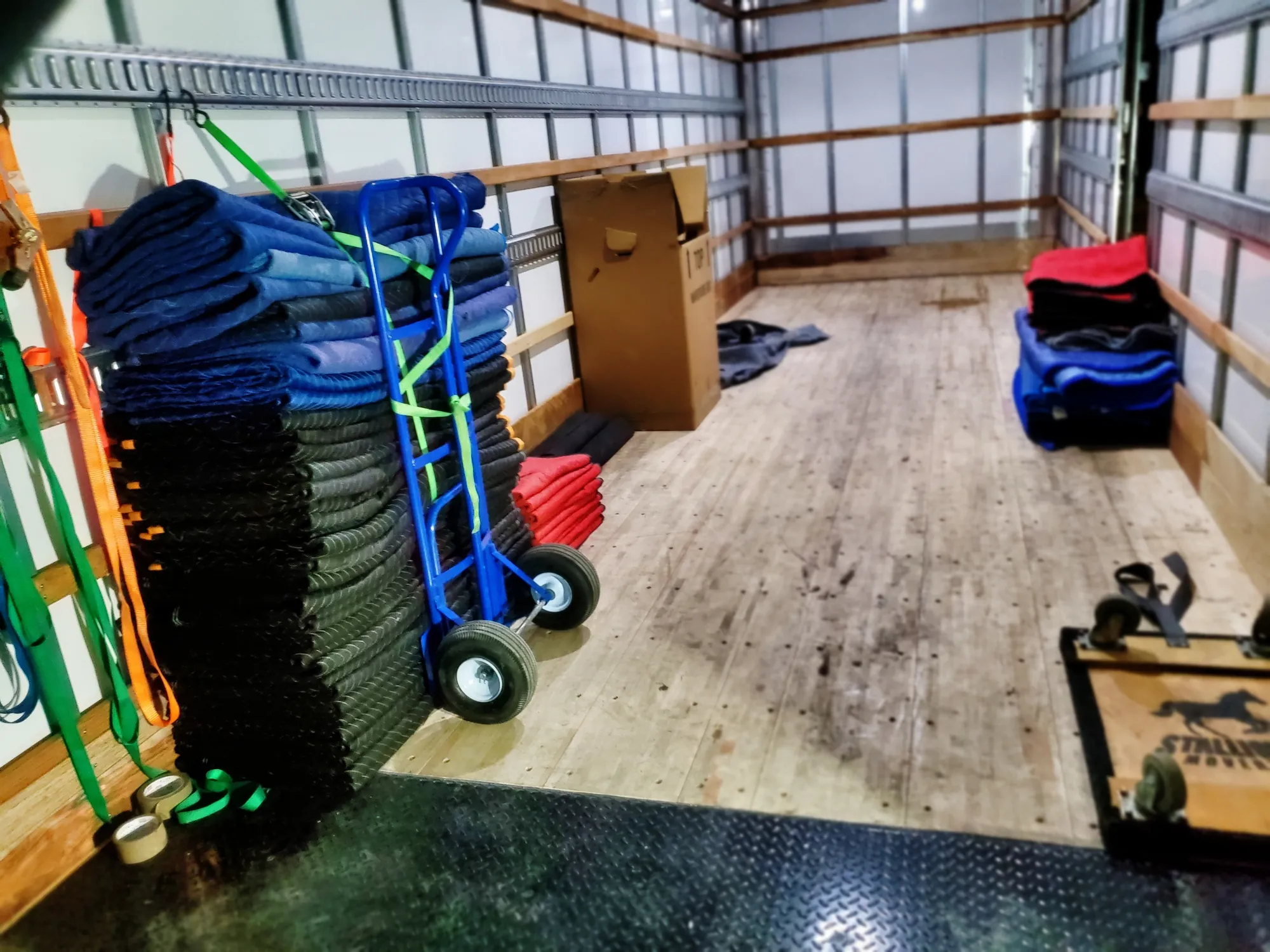 Inside a clean Stallion truck: stacks of folded moving blankets, a hand truck, straps and a Stallion dolly ready for the move
