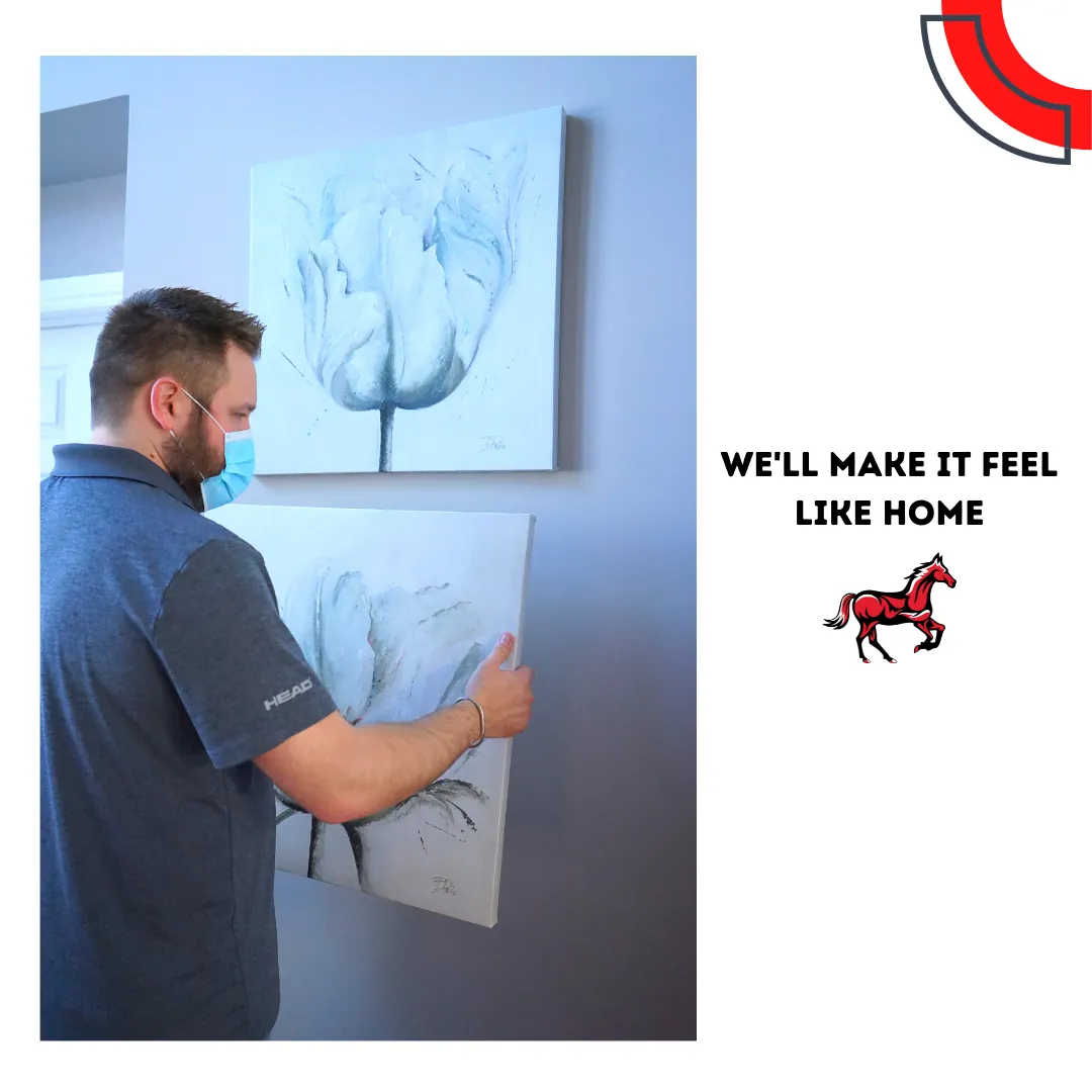 A Stallion team member in a face mask hanging a framed floral canvas on a wall beneath a matching one, beside the words "We'll make it feel like home"