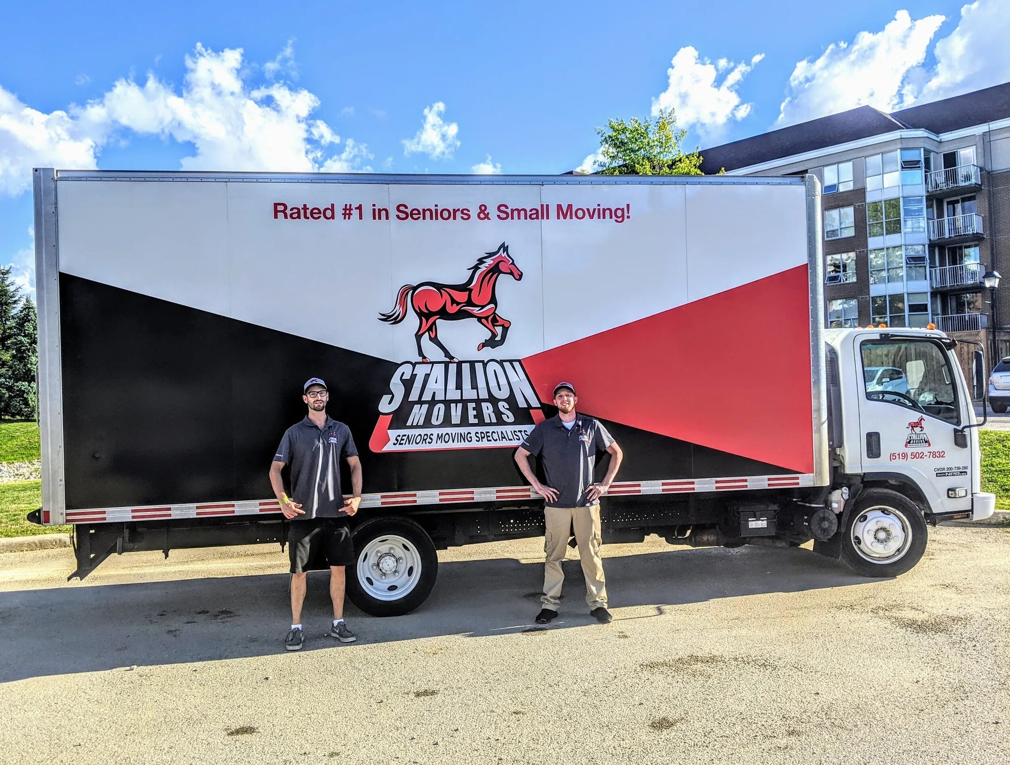 Two uniformed Stallion movers standing in front of a branded Stallion moving truck outside an apartment building
