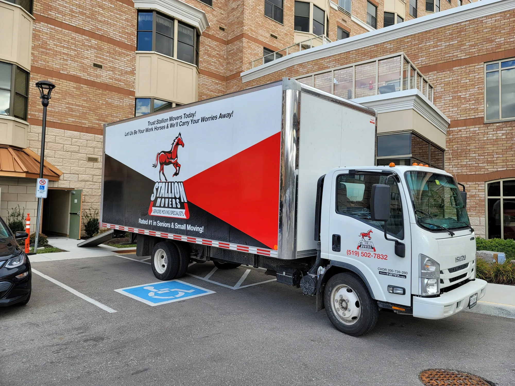 A Stallion moving truck parked in an accessible bay with its ramp down at the entrance of a brick residential building