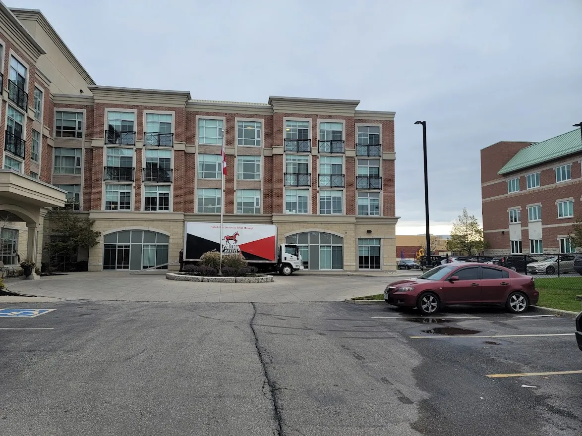 A Stallion moving truck parked at the front entrance of a four-storey brick residential building, seen across an empty car park